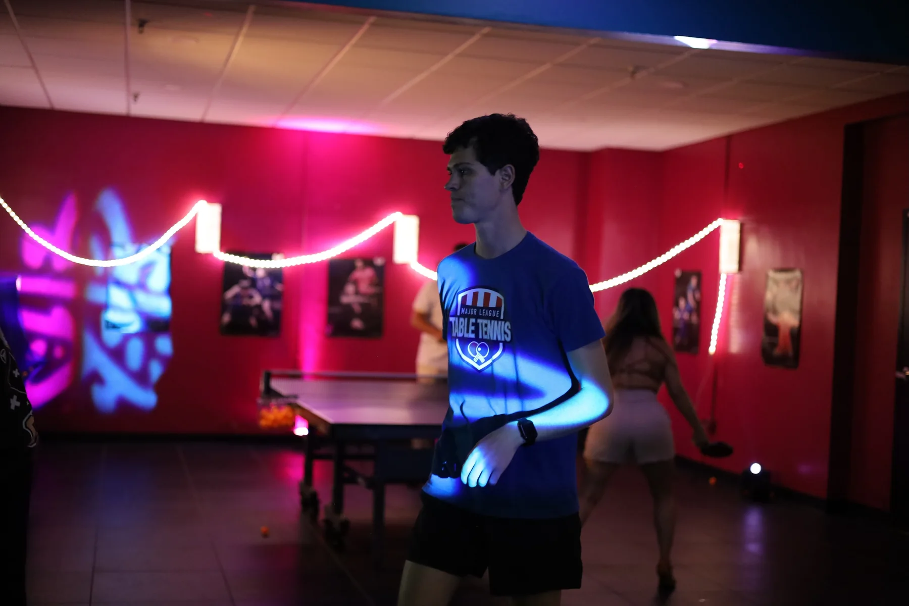 A player at the table against the magenta wall, under a rope of neon light